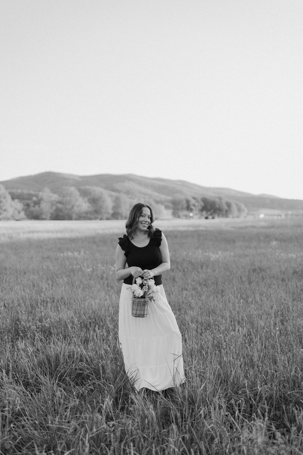 Black and white photo of a woman holding flowers in a mountain meadow wearing contrasting outfit.  Virginia graduation/senior session.