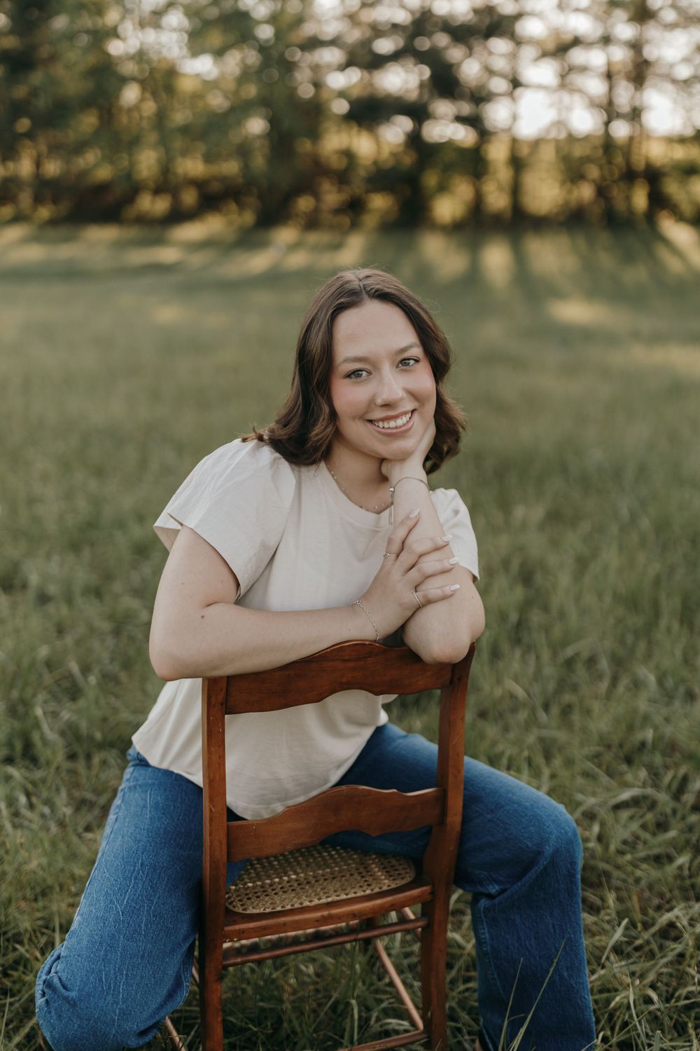 Casual portrait on vintage wooden chair in sunlit meadow. Virginia graduation/senior session.