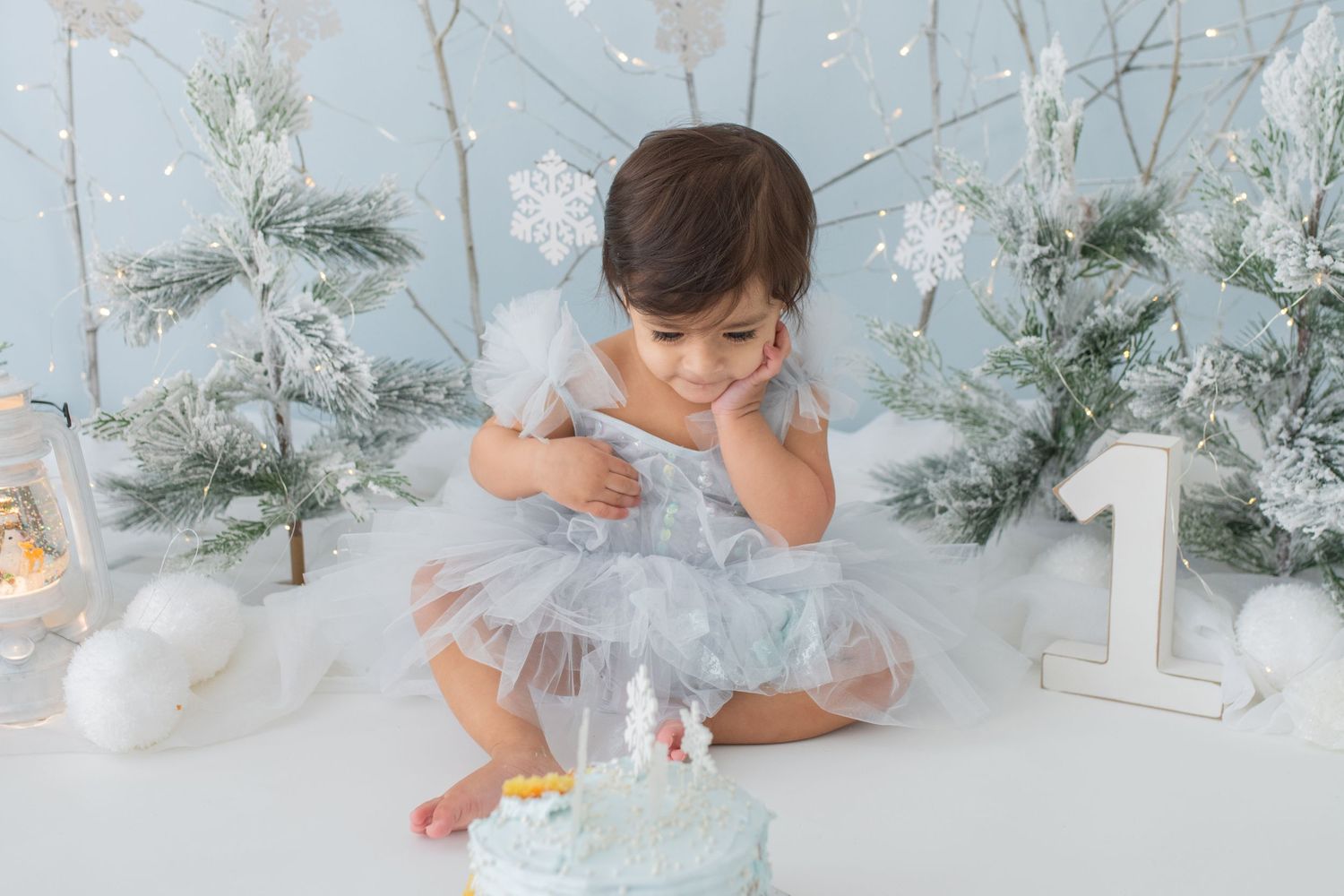 A beautiful girl in a blue dress enjoying a Frozen-themed cake smash setup, creating magical and memorable moments for her 1st birthday!