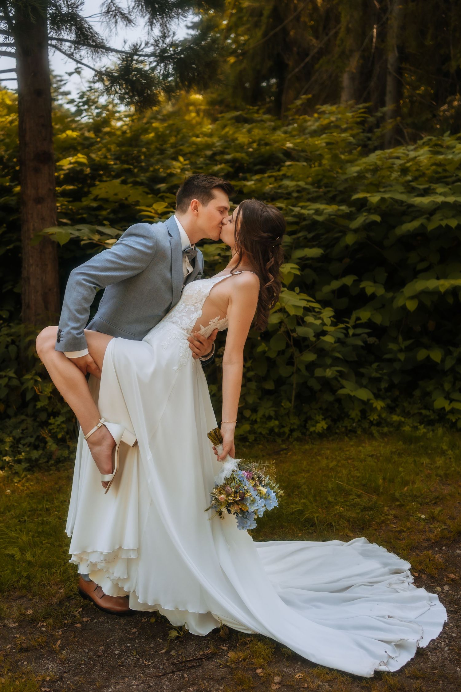 Romantic golden hour wedding photo of a couple kissing in a field with sun rays and trees in the background.