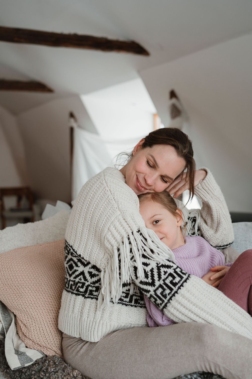 A tender moment of rest and cuddles in a cozy attic room with exposed wooden beams and soft textiles.  Fotografering Karlskrona