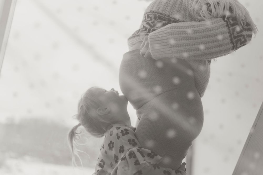 Black and white artistic maternity photo in dim lighting showing silhouette and shadows.