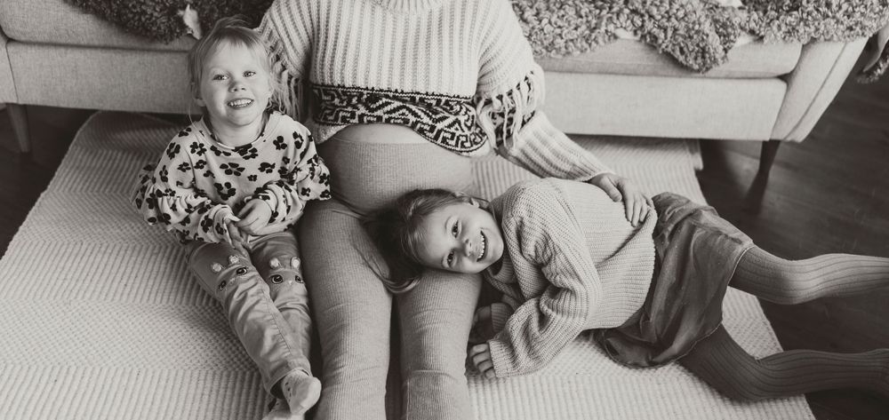 Black and white photo showing two children relaxing on parent's lap in a casual home setting.