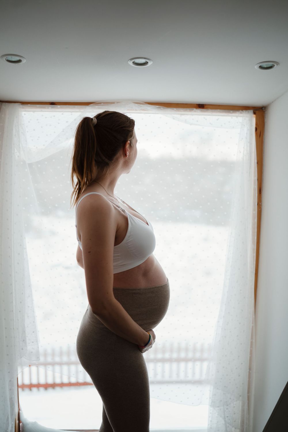 Silhouette of pregnant woman in athletic wear standing by window.