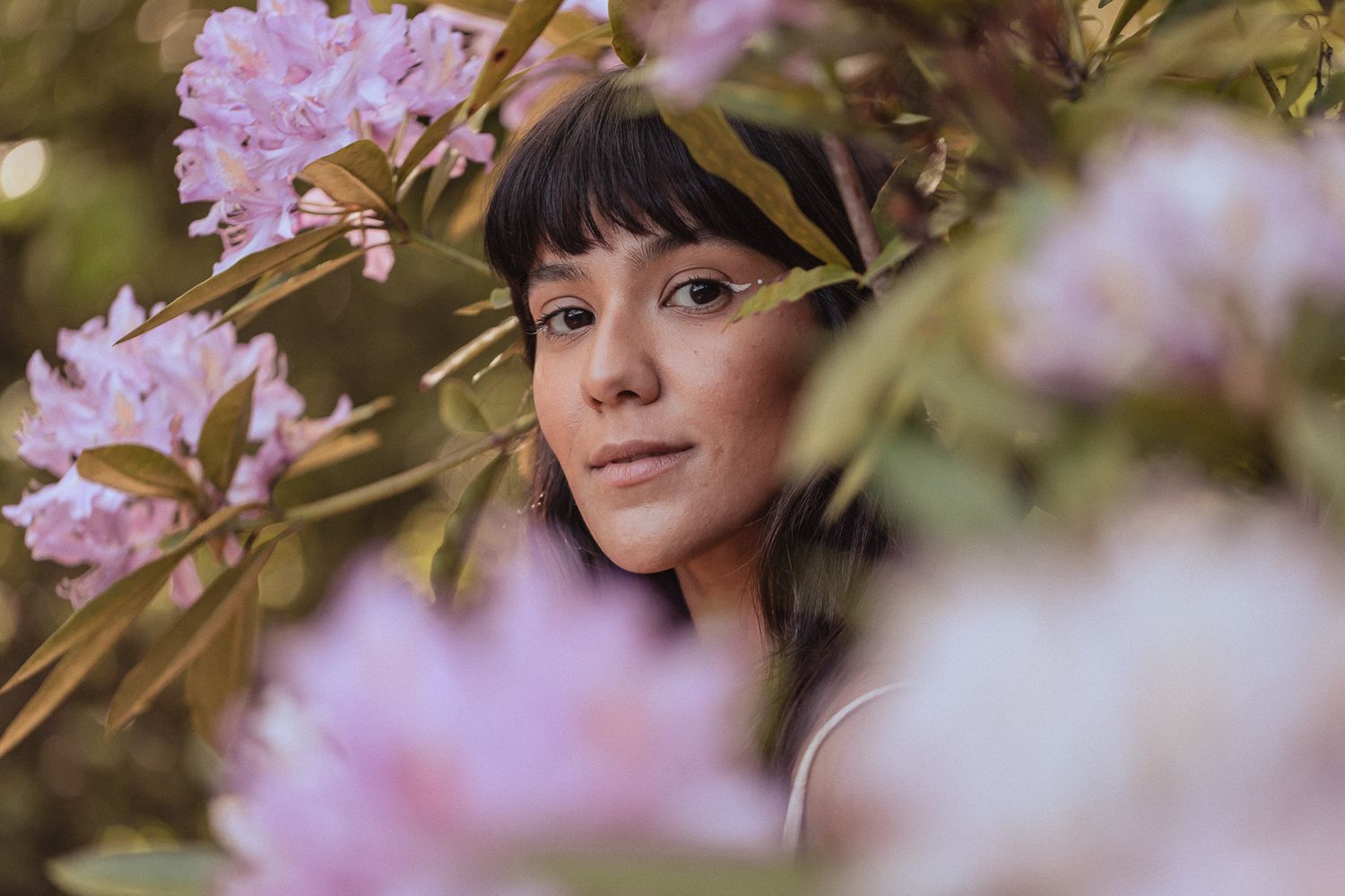 A portrait among blooming pink rhododendron flowers with soft natural bokeh in the background.