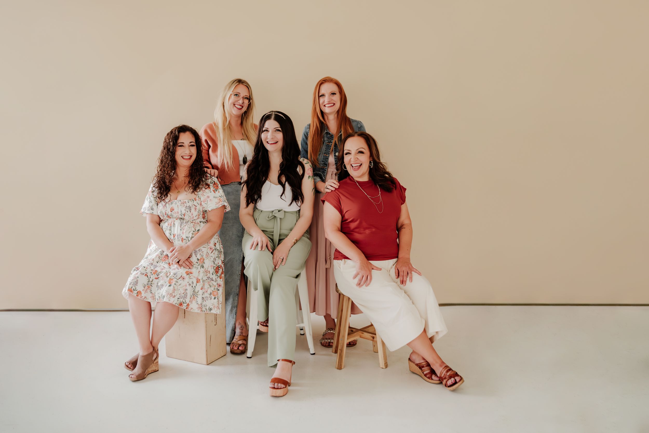 A professional lifestyle photo of a small group seated together in light casual attire against a neutral backdrop.