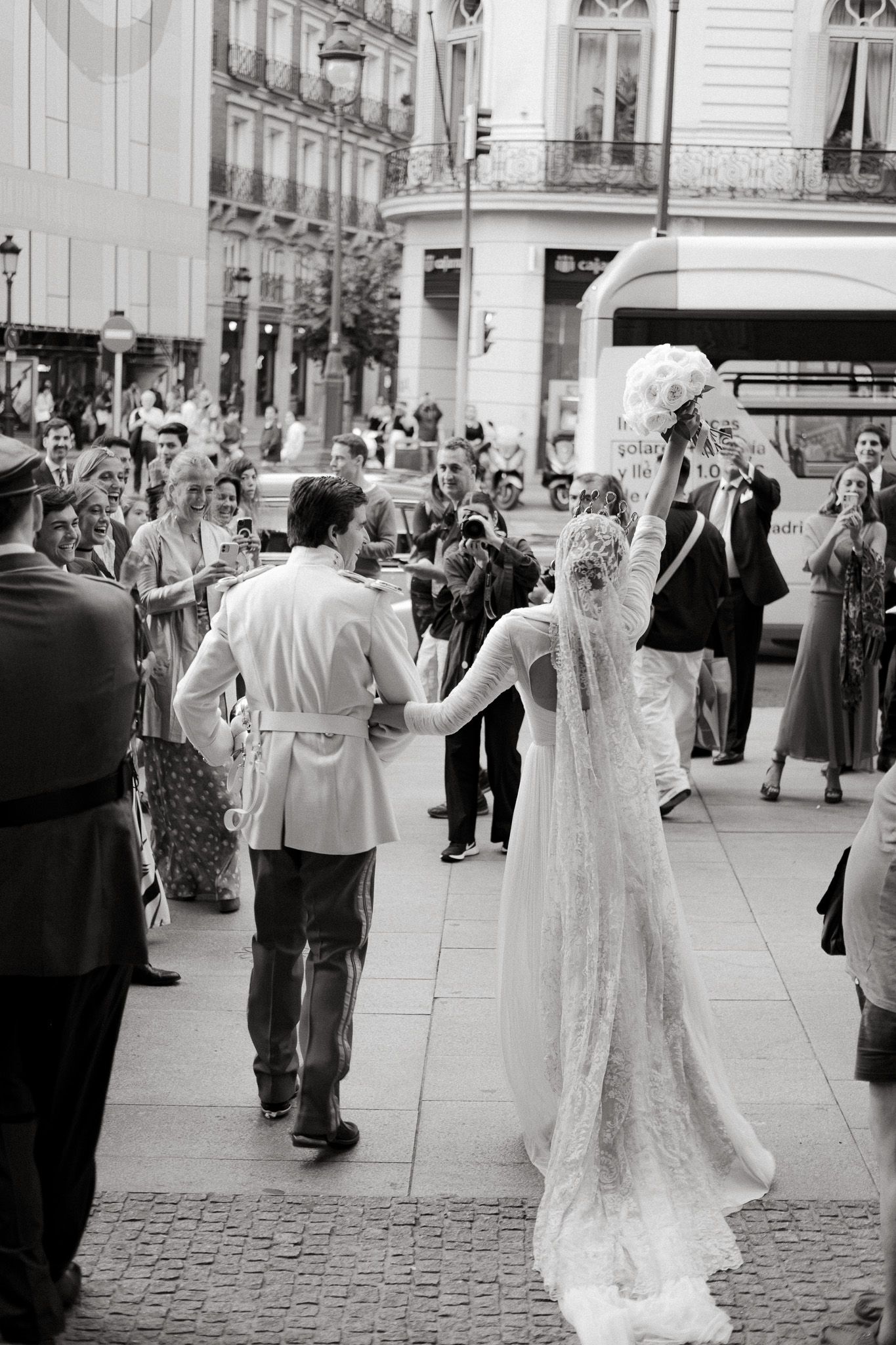 Couple walking down a cobblestone street during a wedding celebration with guests looking on.