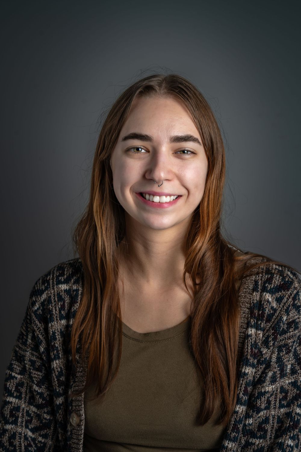 Studio portrait against dark grey background wearing patterned cardigan.