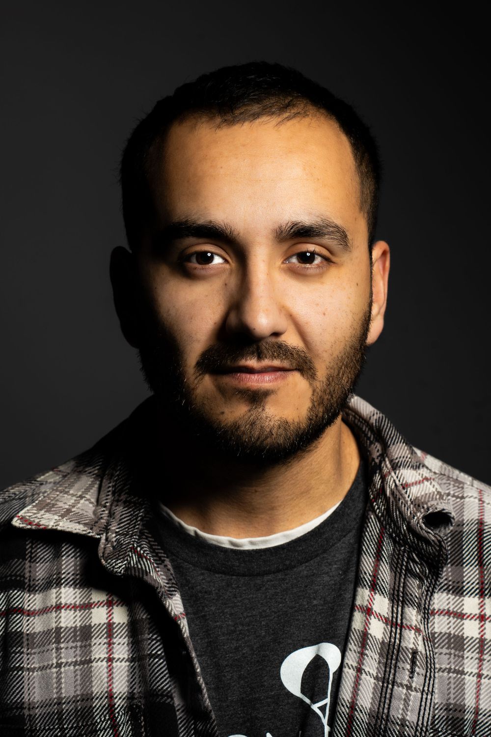 Studio portrait against dark background wearing plaid flannel shirt.
