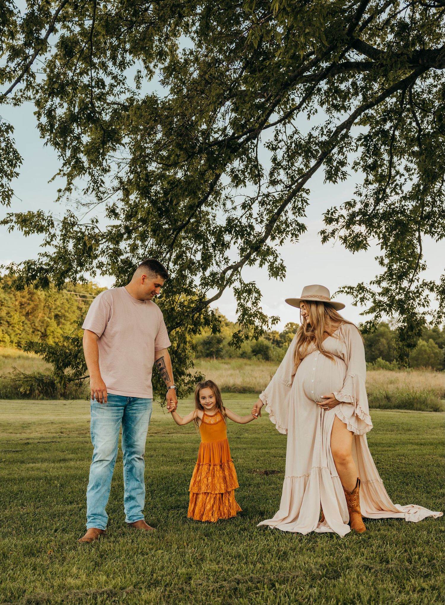 Family in light colored outfits standing together in a grassy field at sunset. rockford il senior photographer