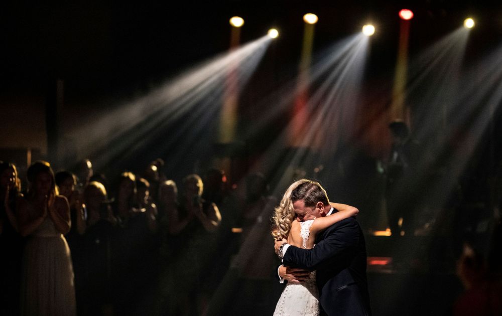 Couple sharing an intimate dance moment under colorful stage lighting at their reception.