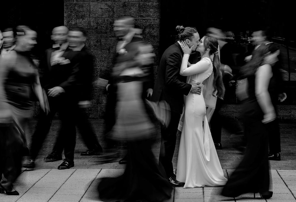 Motion blur photo of couple kissing while others walk past in black and white.