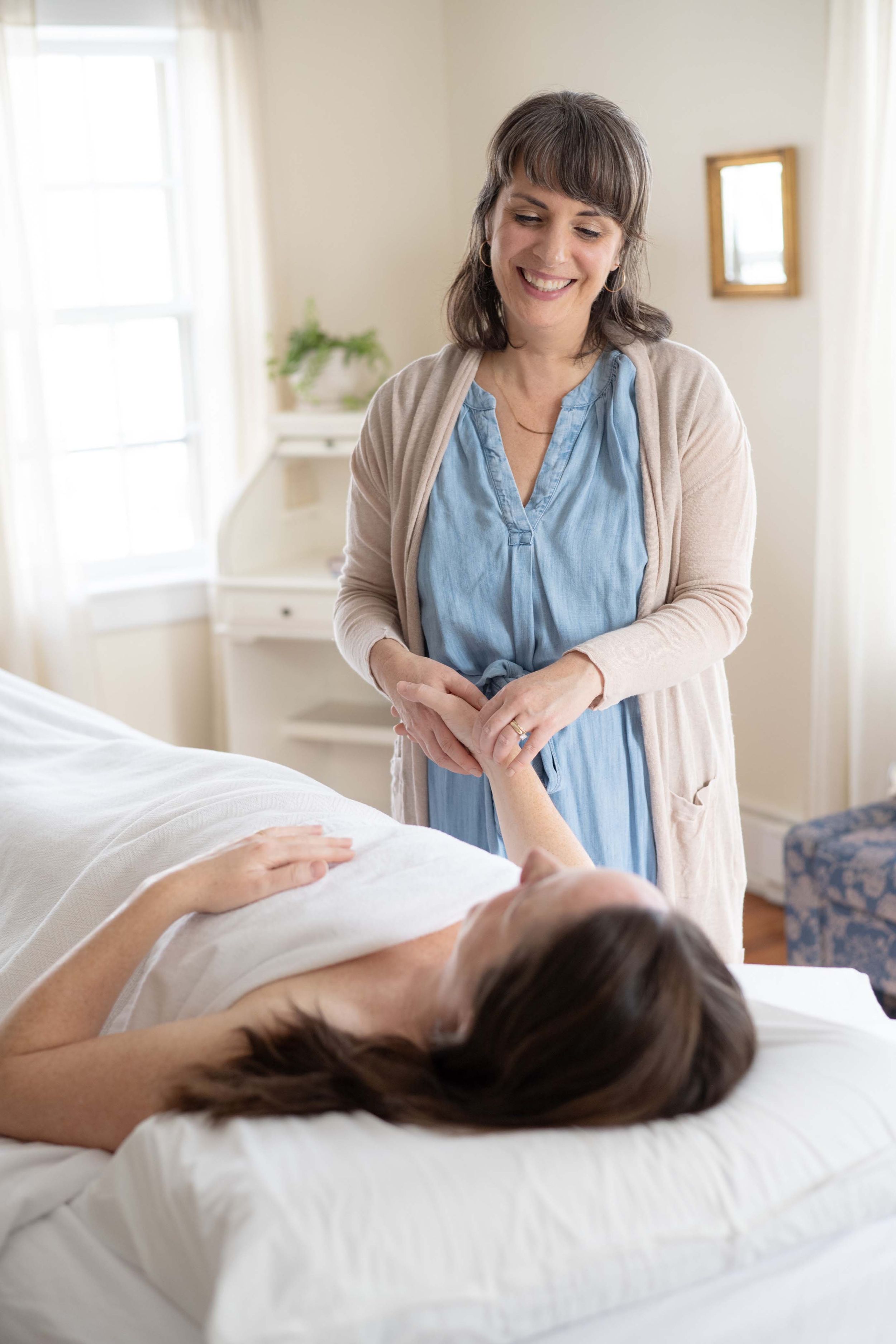 A massage therapist in muted tones provides therapeutic treatment in a bright, peaceful spa room setting.