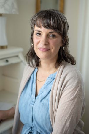 Portrait of someone in a beige cardigan and blue blouse smiling warmly in a bright indoor setting.