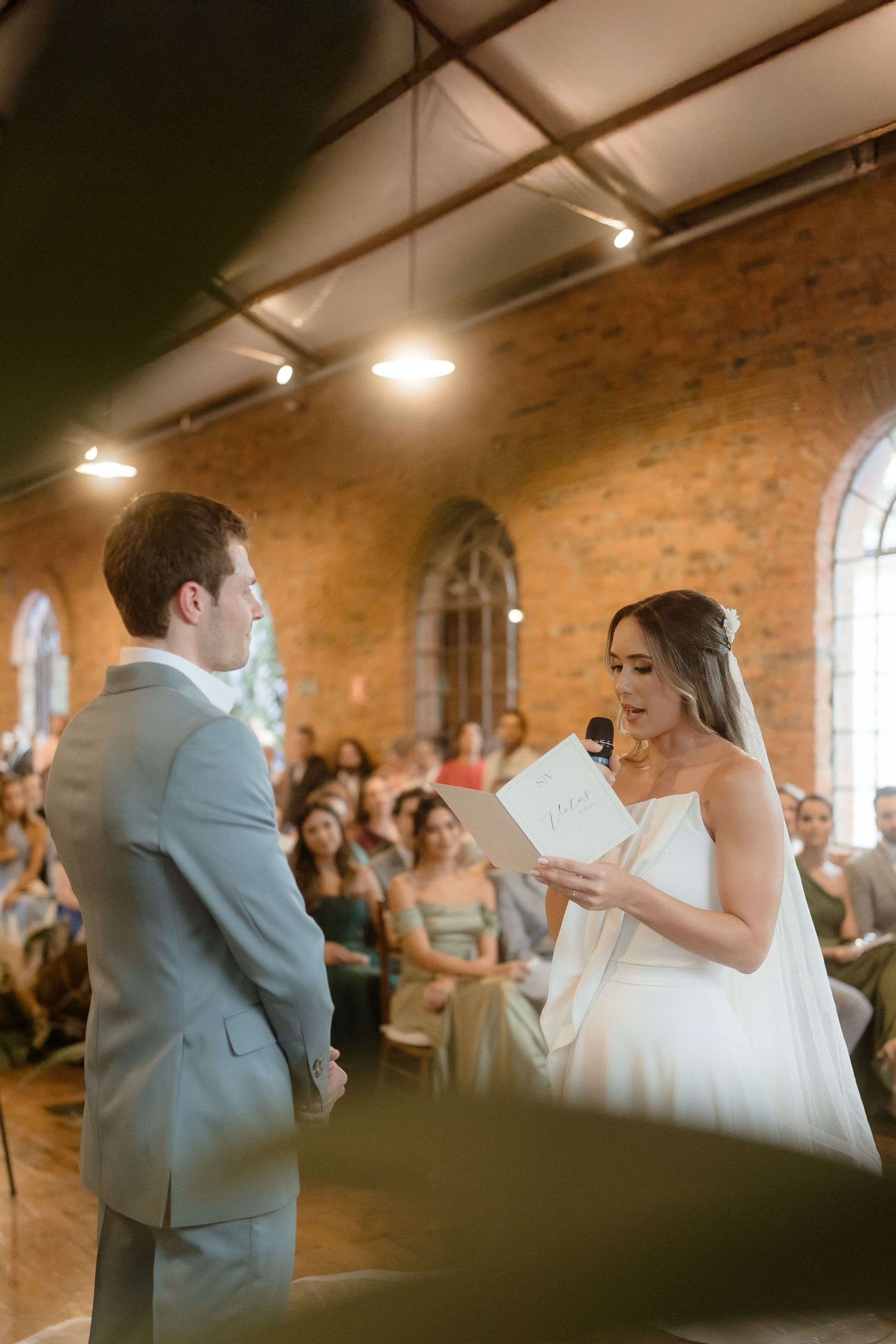 Couple exchanges vows in beautiful brick venue with arched windows and warm lighting.