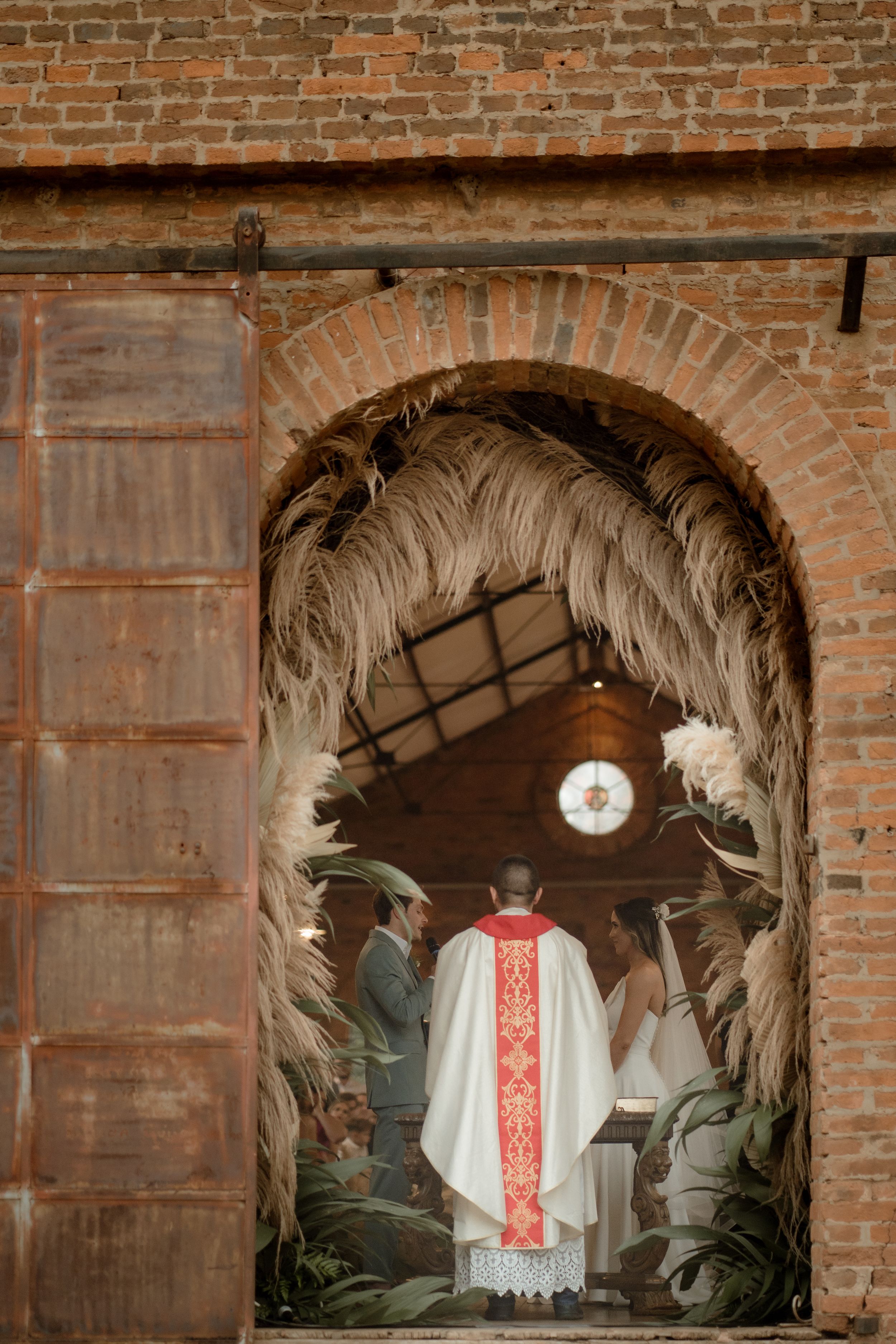 Ornate dried palm arch frames officiant during wedding ceremony in historic brick church.