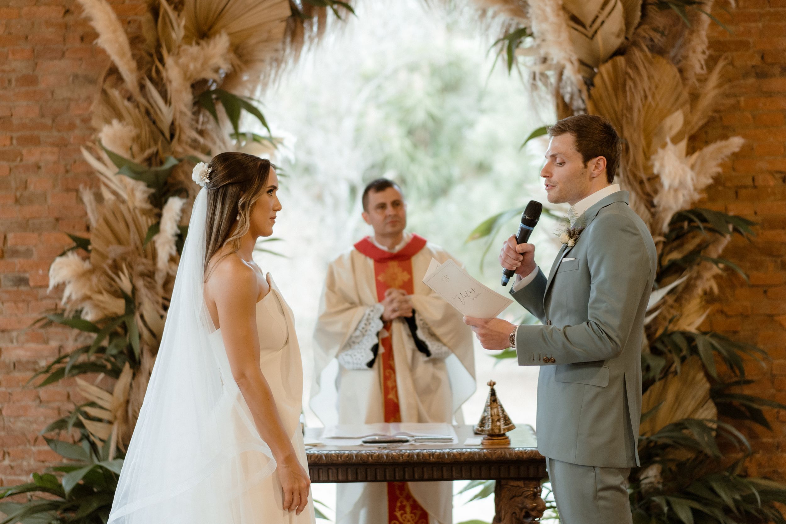 Wedding ceremony under dried palm arch with officiant and couple exchanging vows.