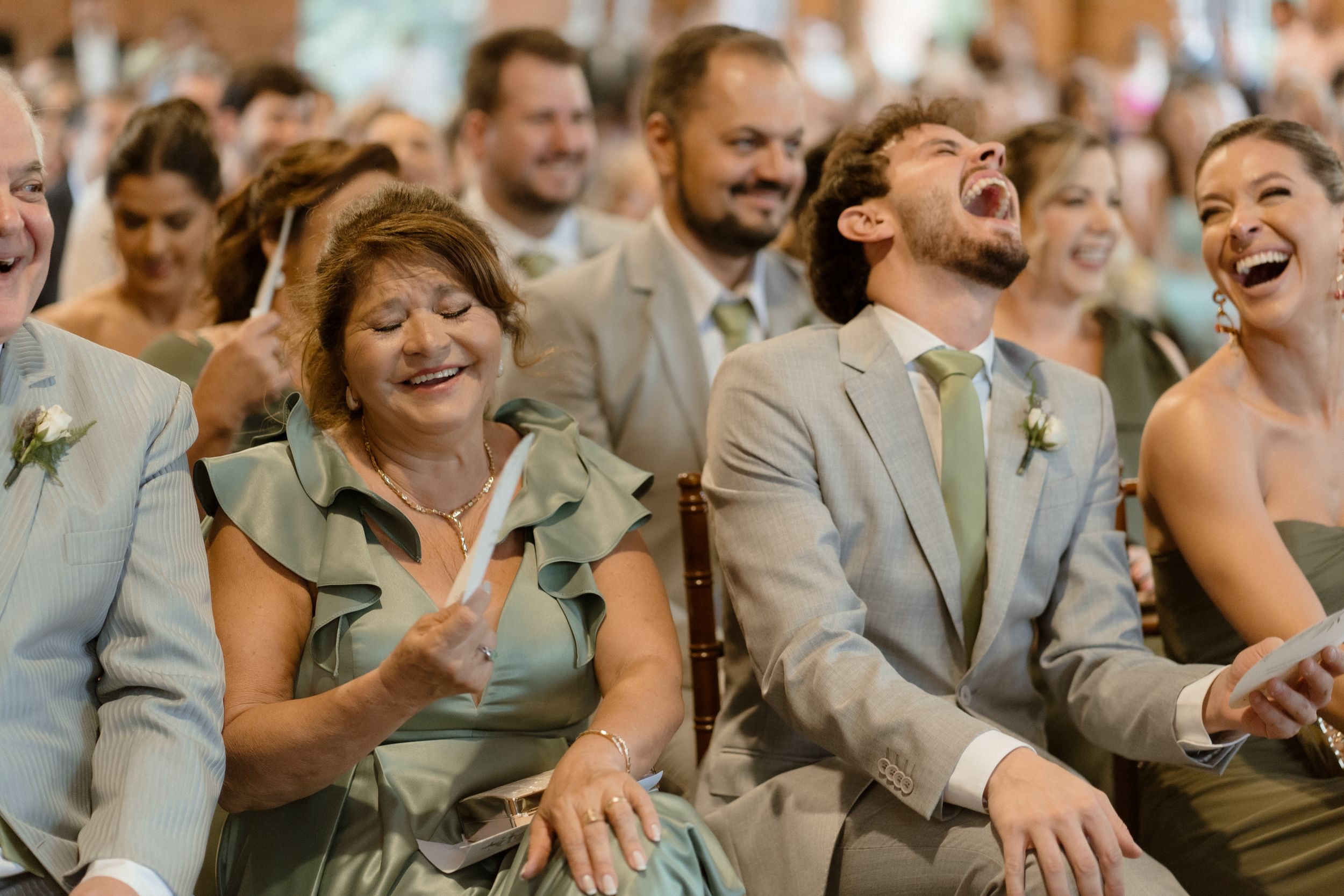 Wedding guests in formal attire share genuine laughter during ceremony.