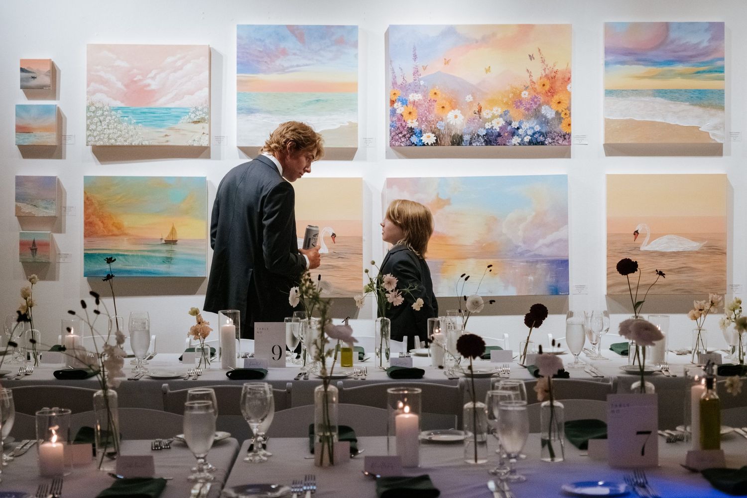 Wedding reception setup with ethereal watercolor art displays and elegant table settings.