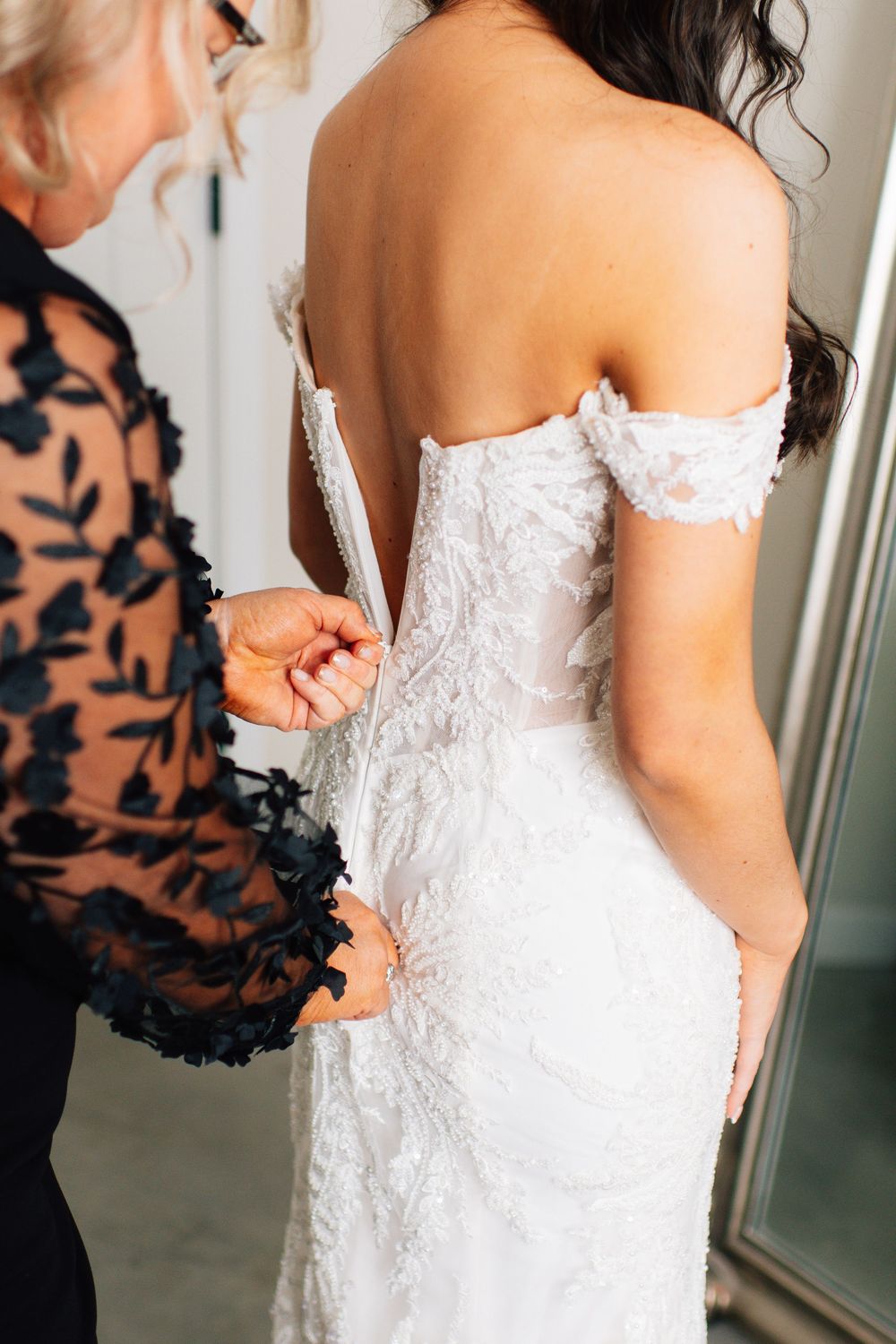 Close-up of intricate lace details being fastened on back of white wedding dress.