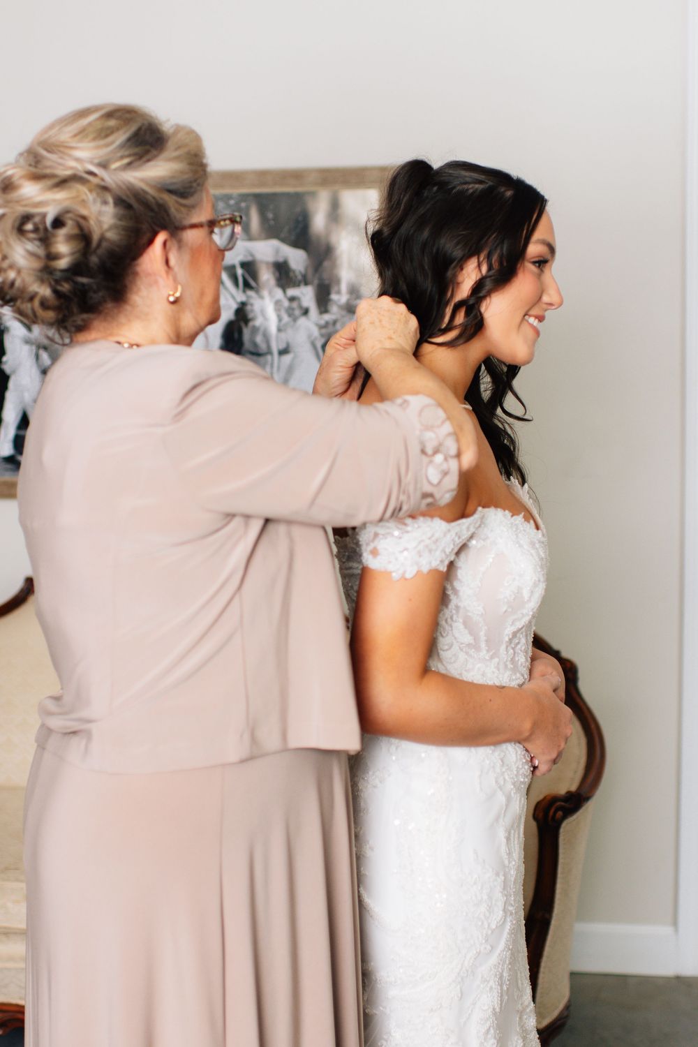 Tender moment as family member in beige dress helps bride with wedding preparations.