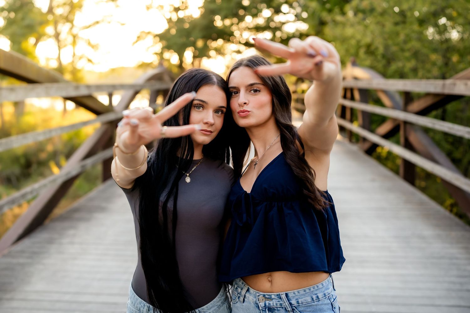 Two people pose playfully on a wooden boardwalk during golden hour sunset lighting.
