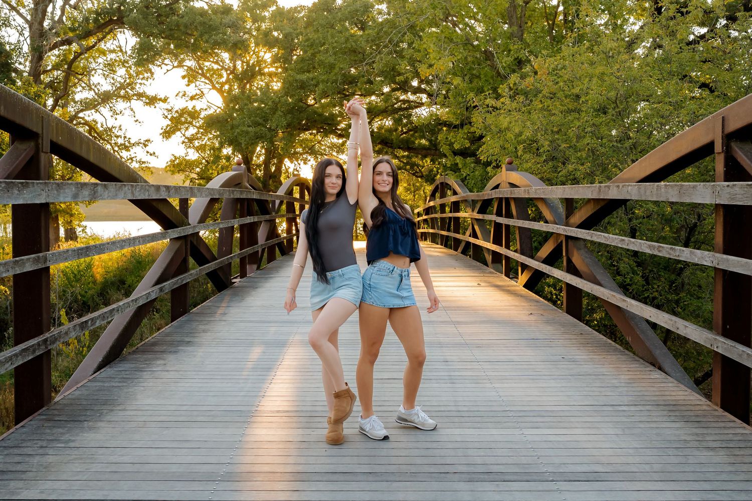 Wooden footbridge in a park during golden hour with sunlight filtering through trees.