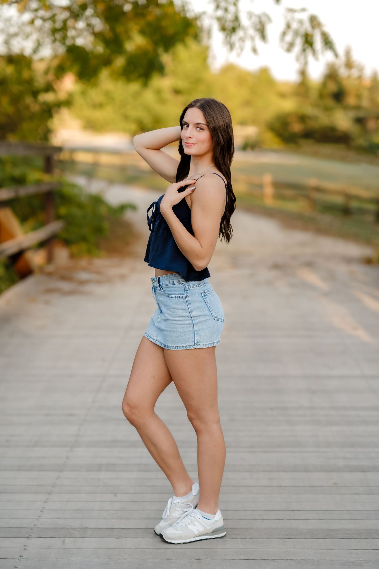 A woman in denim shorts and black top poses on a wooden boardwalk during golden hour.