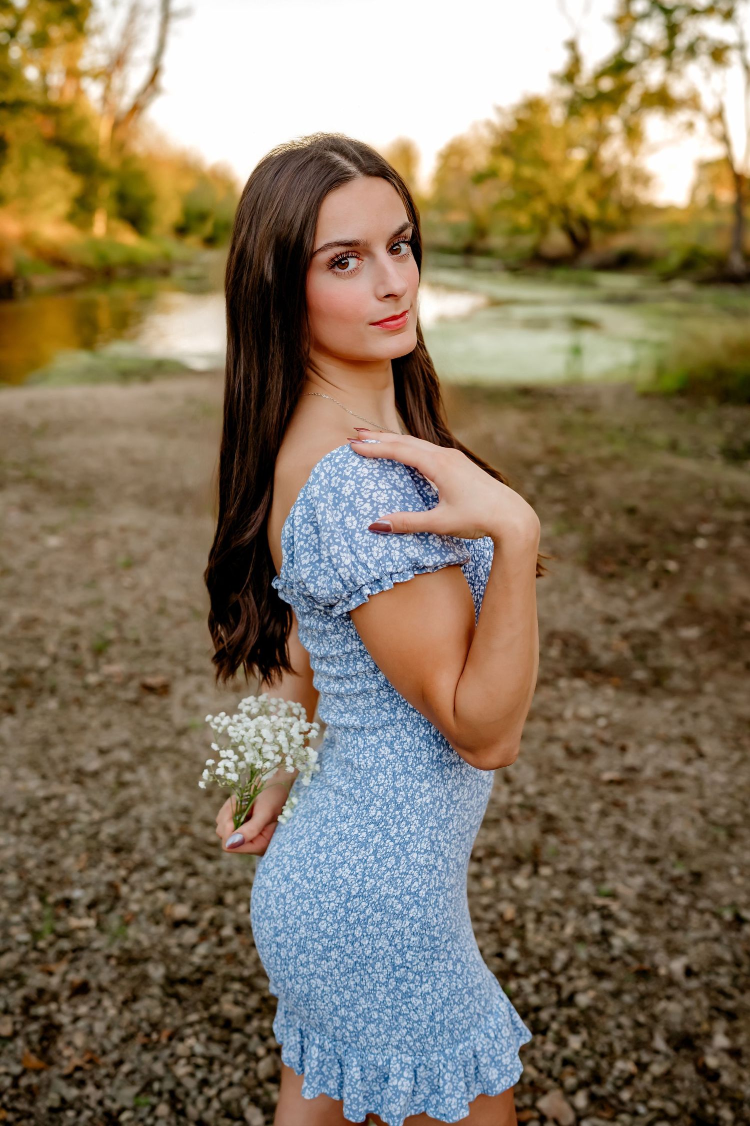 Light floral dress worn in an outdoor setting with autumn trees and water in the background.
