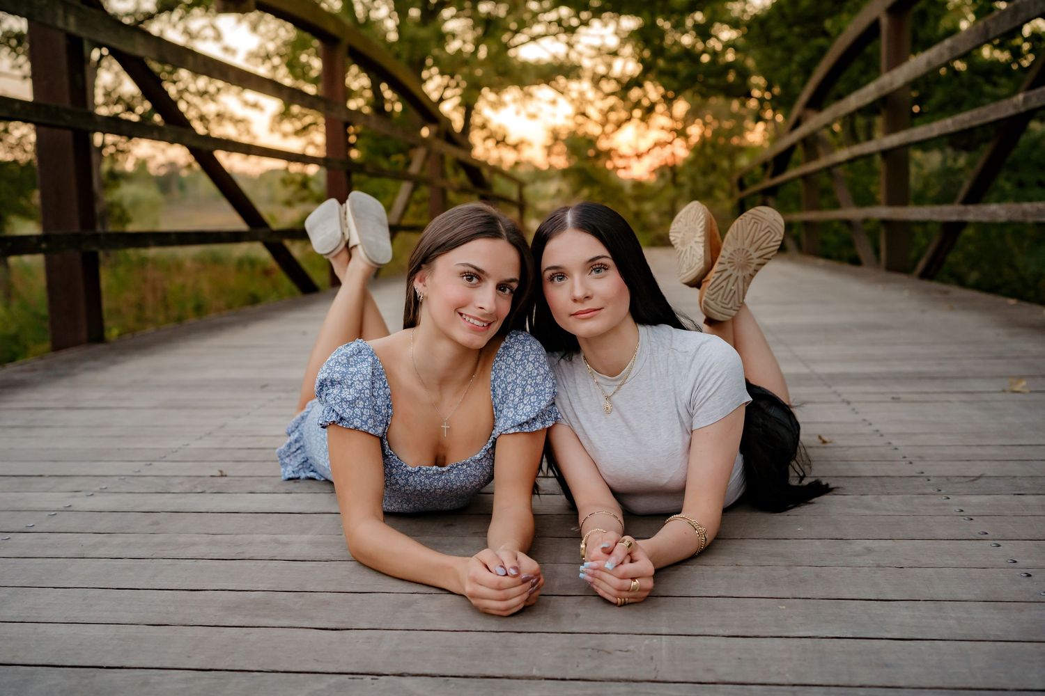 Two people lying on wooden bridge deck at sunset creating playful poses for photos.