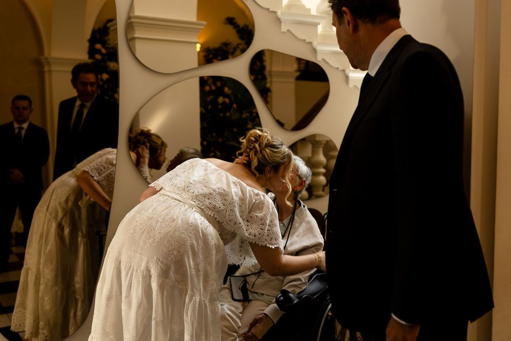 Wedding guests in formal attire gather at an elegant indoor reception venue with white decor and lighting.