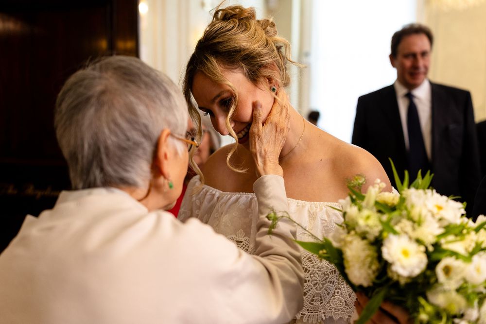 An emotional moment between a bride in a white dress and an elderly person at a wedding, with a bouquet of white flowers.