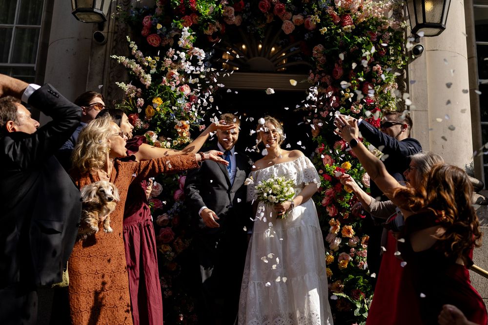 Wedding guests throwing flower petals and confetti in celebration outside a building.