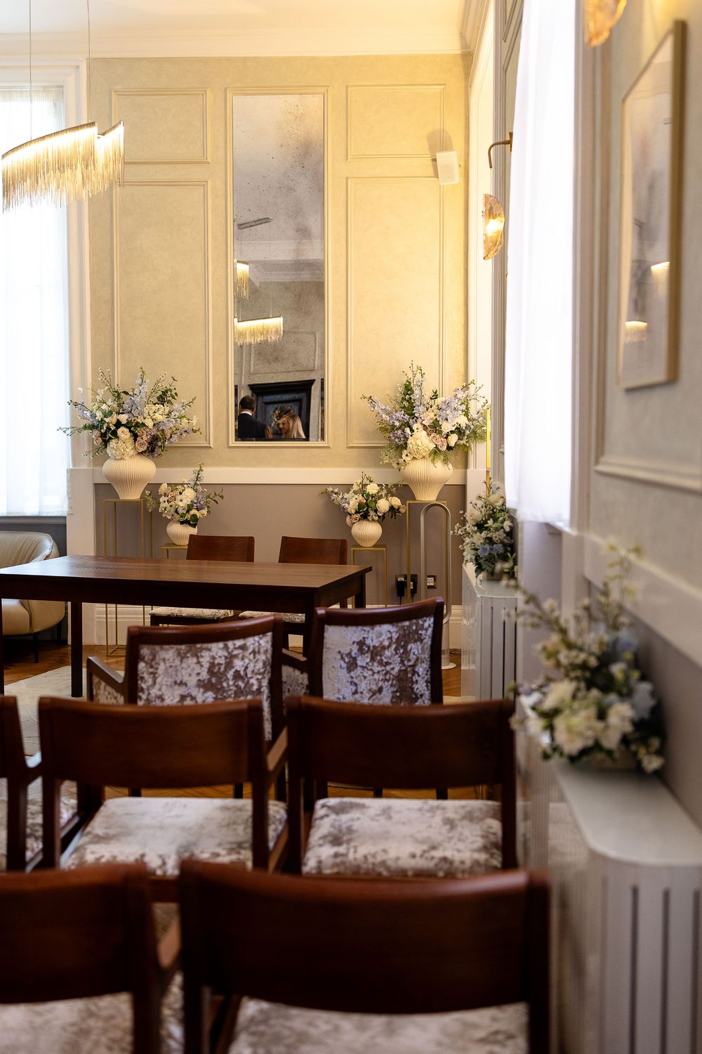 Elegant dining room with white walls, dark wood furniture, and floral arrangements on display.