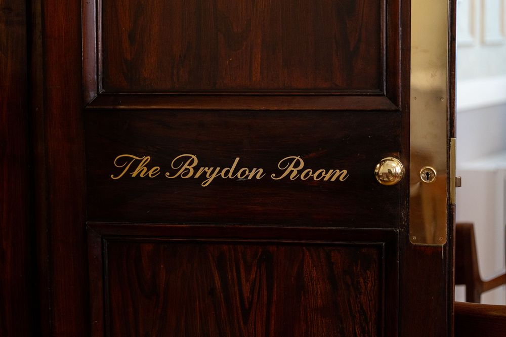 Elegant dark wood-paneled restaurant interior with ornate moldings and 'The Brydon Room' signage illuminated above.