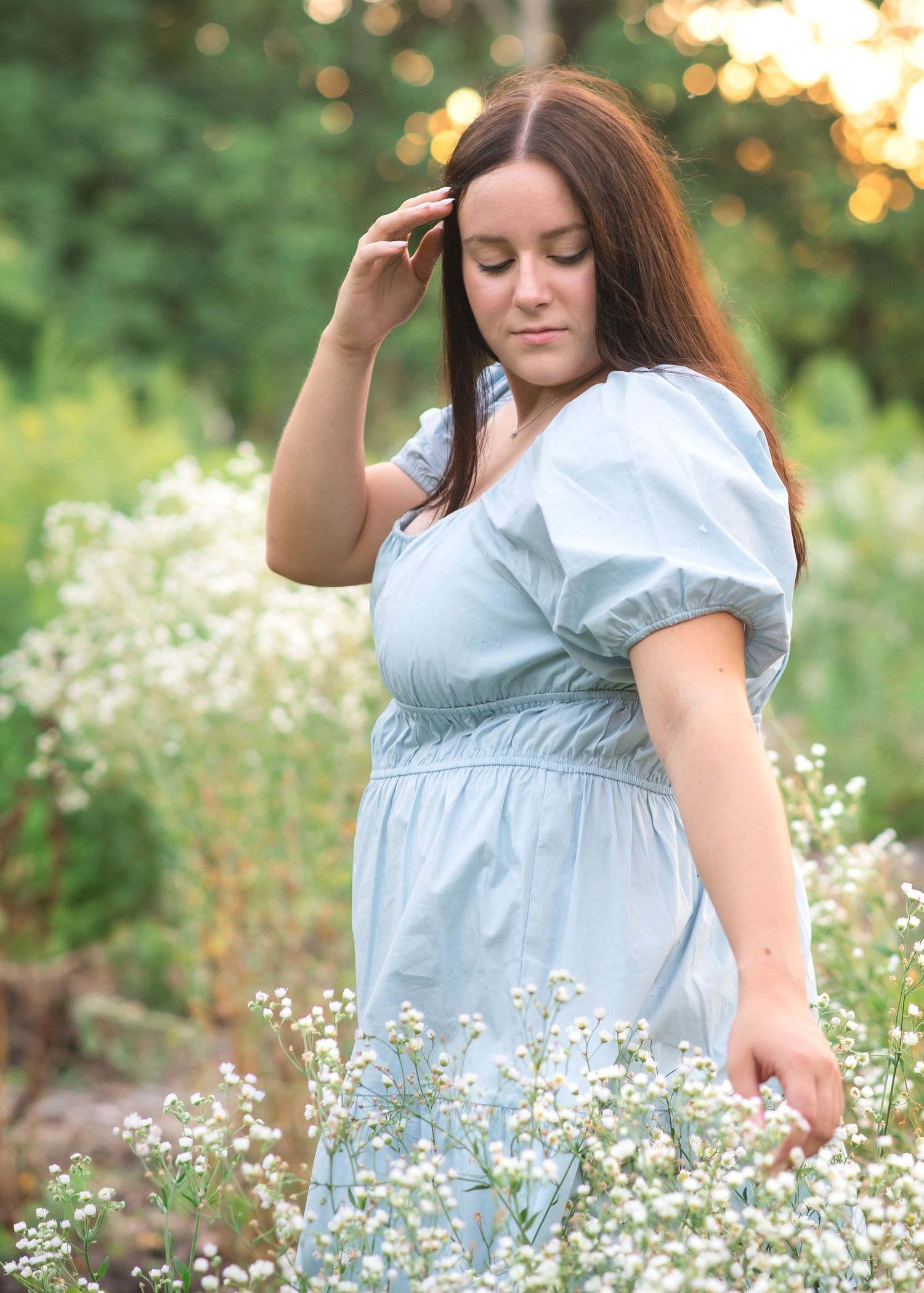 A person in a light blue dress twirls gracefully in a field of white wildflowers during golden hour.