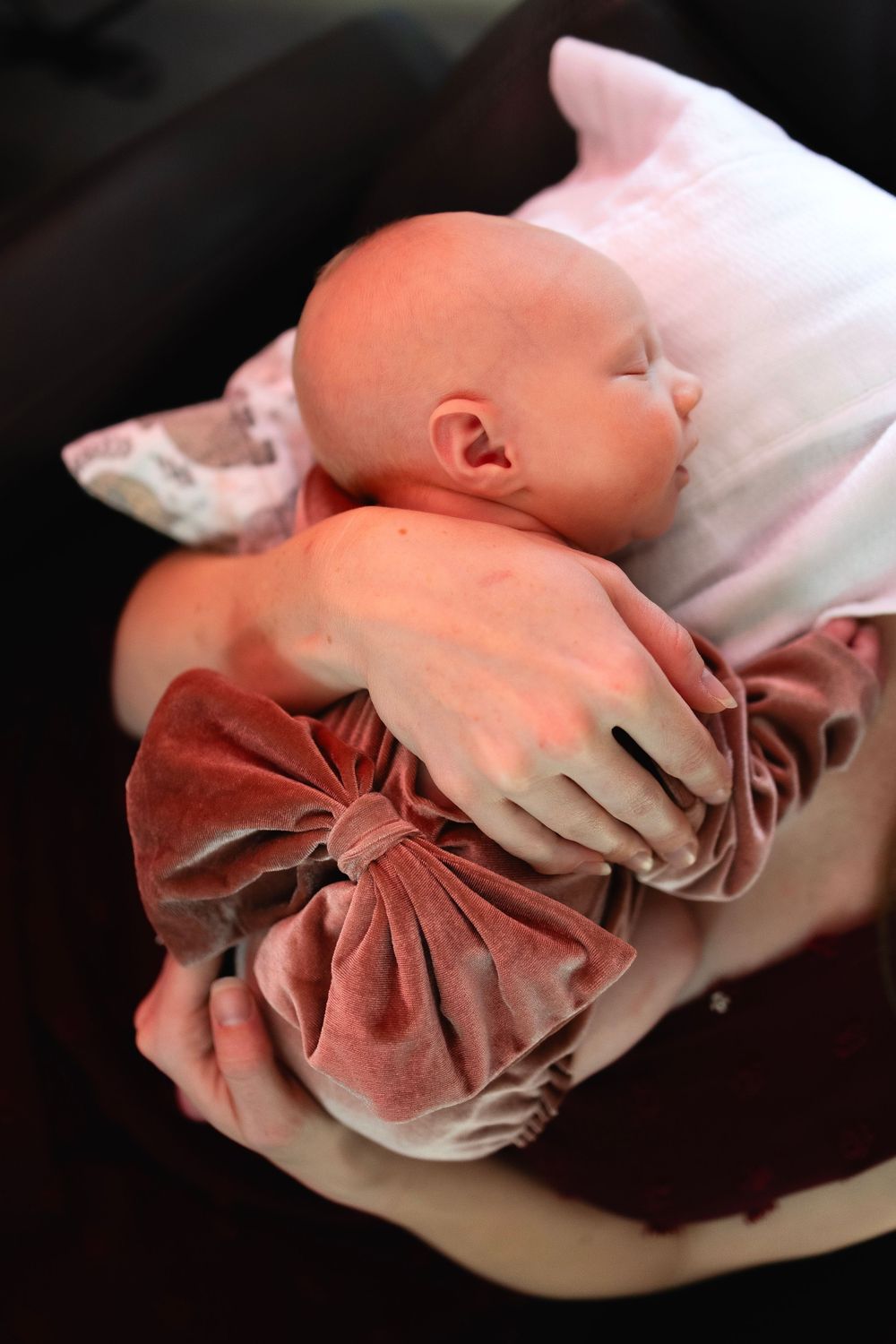 A sleeping infant wearing a velvet dress rests peacefully on white fabric.