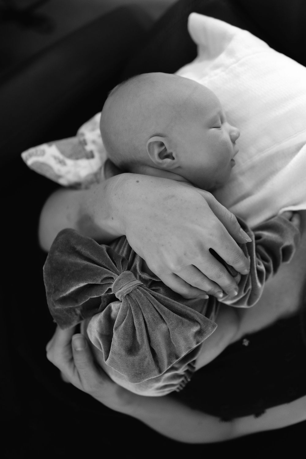 A sleeping baby in a velvet dress rests peacefully on a white pillow in black and white photography.