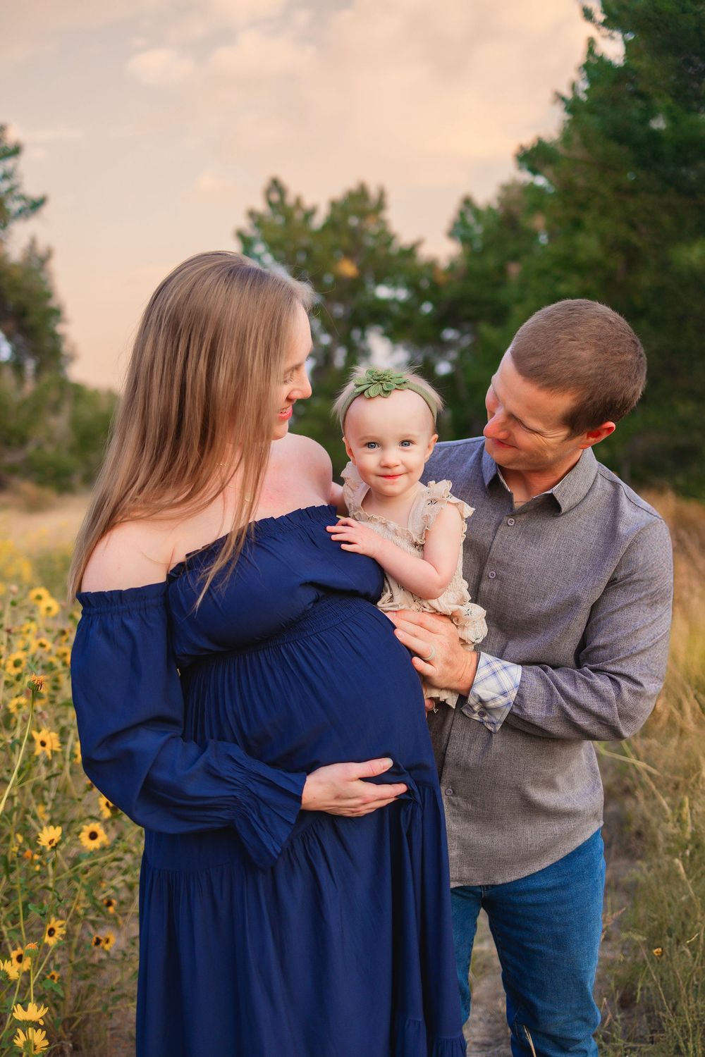 Family of three poses together in a field of wildflowers at sunset in matching navy and gray outfits.