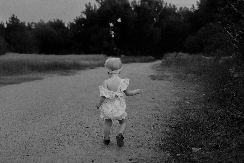 Black and white photo of a small child in a dress walking alone down a rural dirt path.