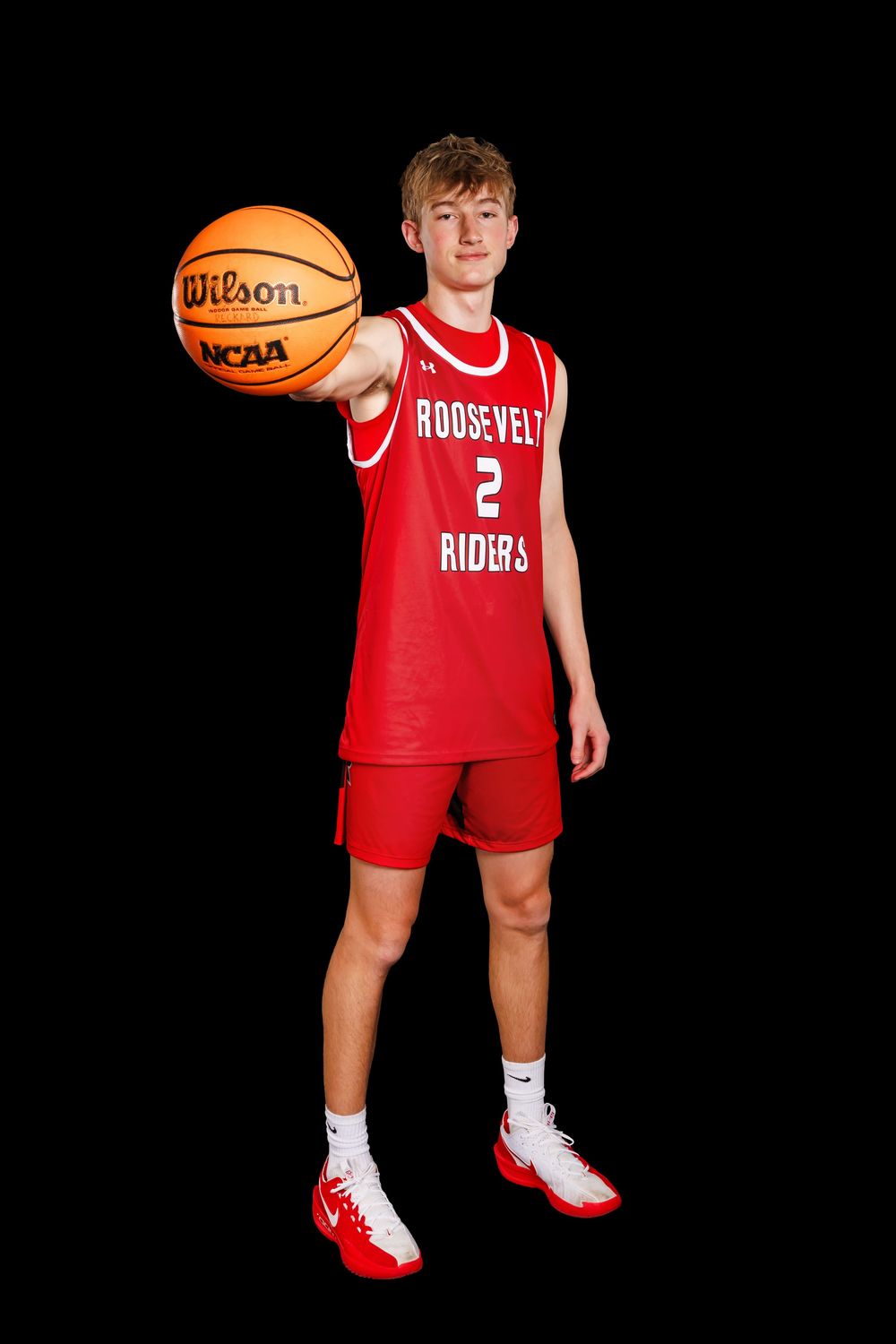 Basketball player in red Roosevelt Riders uniform holds orange ball against black background.