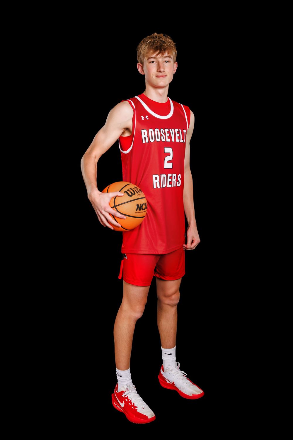 Basketball player in red Roosevelt Riders uniform poses with ball against black background.