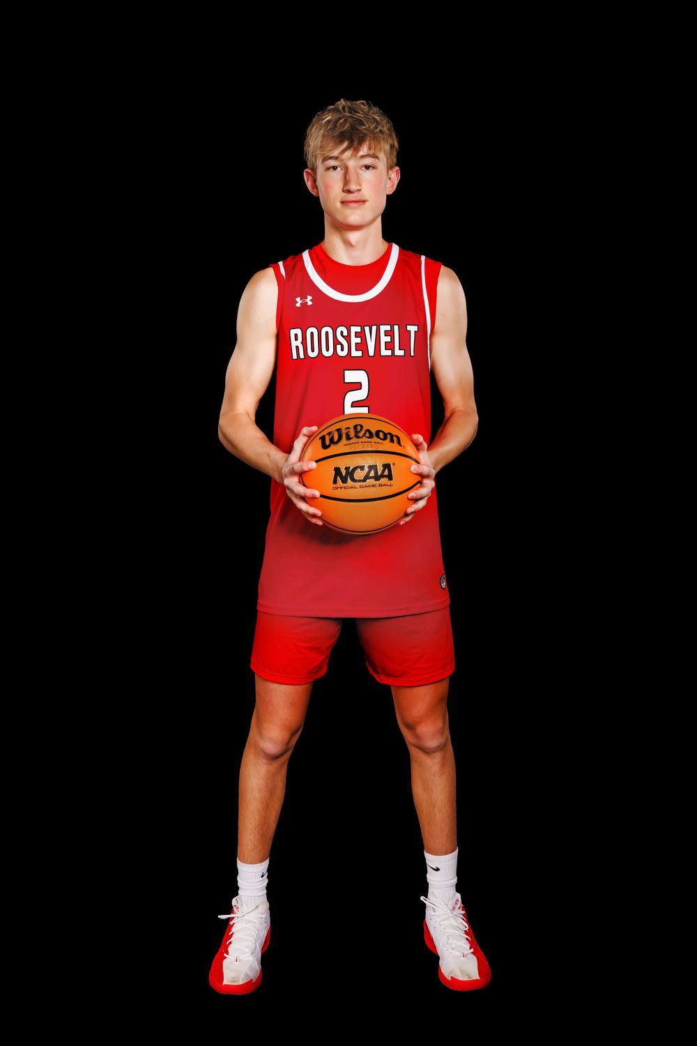 Basketball player in red Roosevelt uniform holds NCAA basketball in classic posed stance against black background.