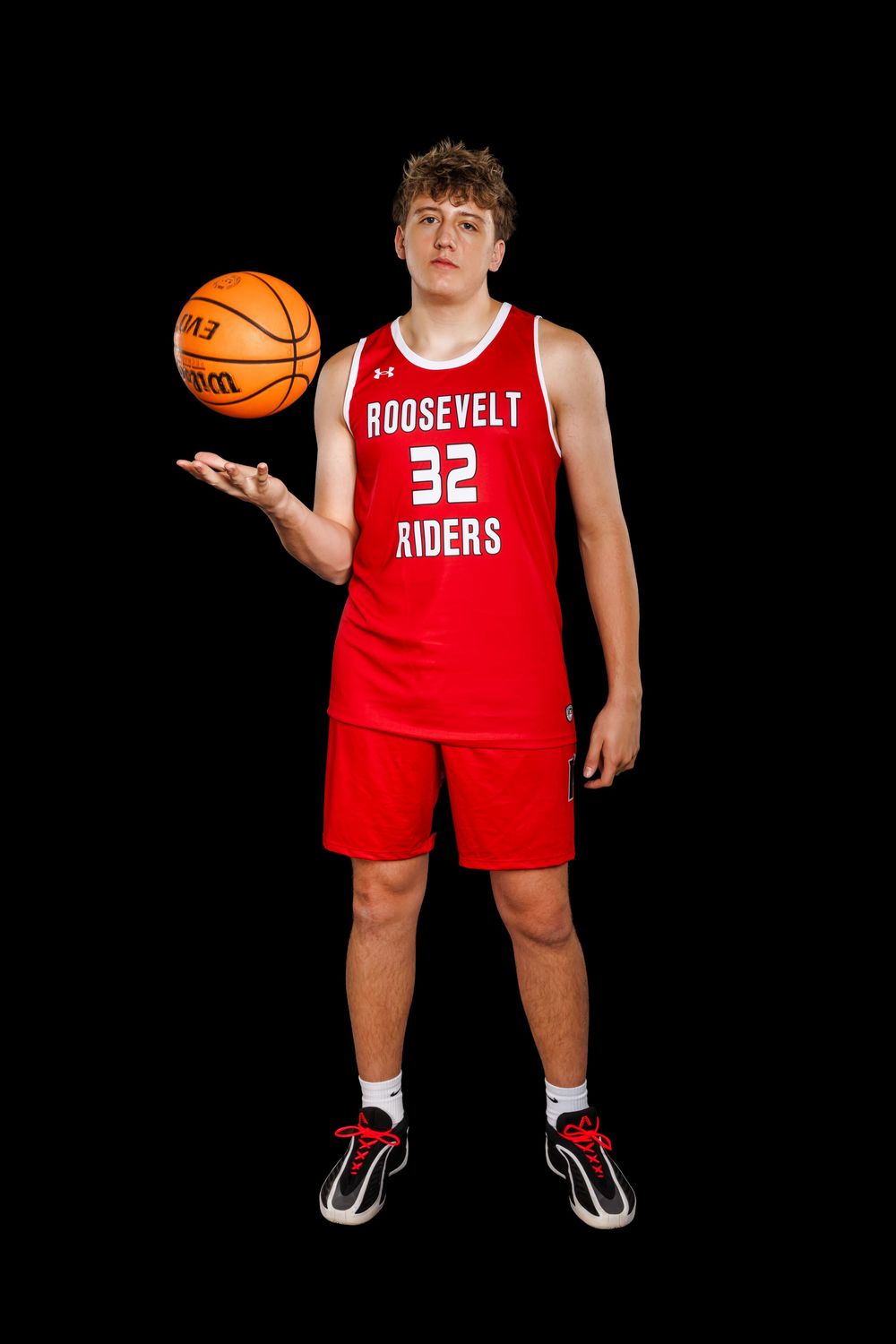 Basketball player in Roosevelt Riders jersey number 32 balances basketball on palm against dark backdrop.