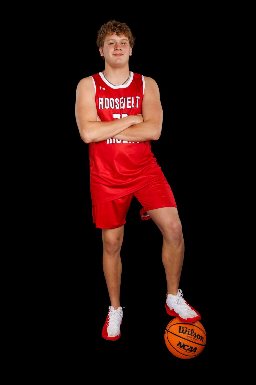 Basketball player in red Roosevelt Riders uniform poses with basketball against black background.