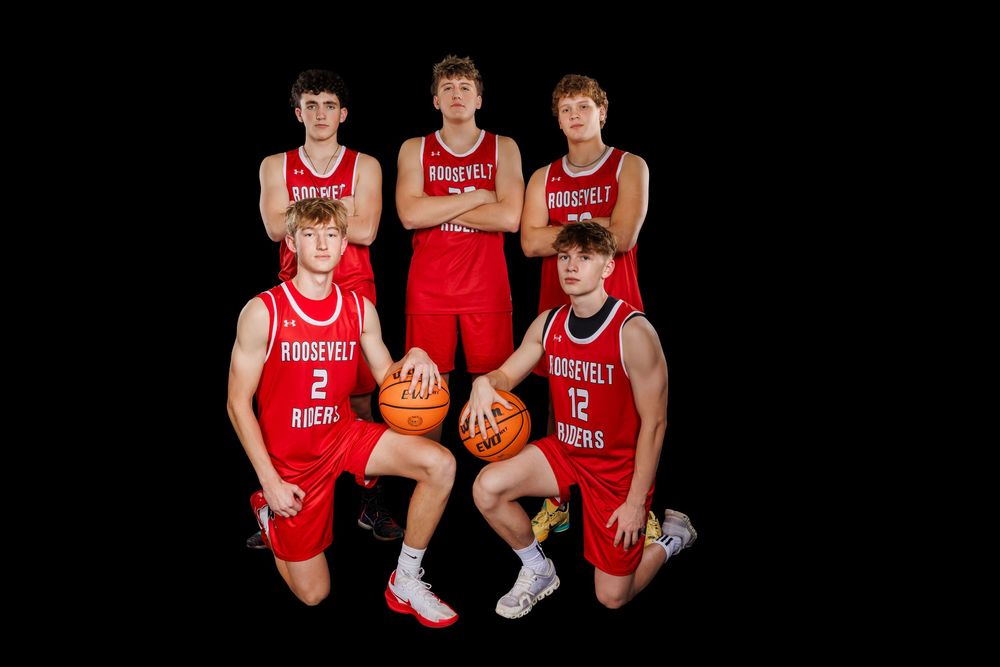 Basketball team members in red and white uniforms pose together for a group photo on dark background.