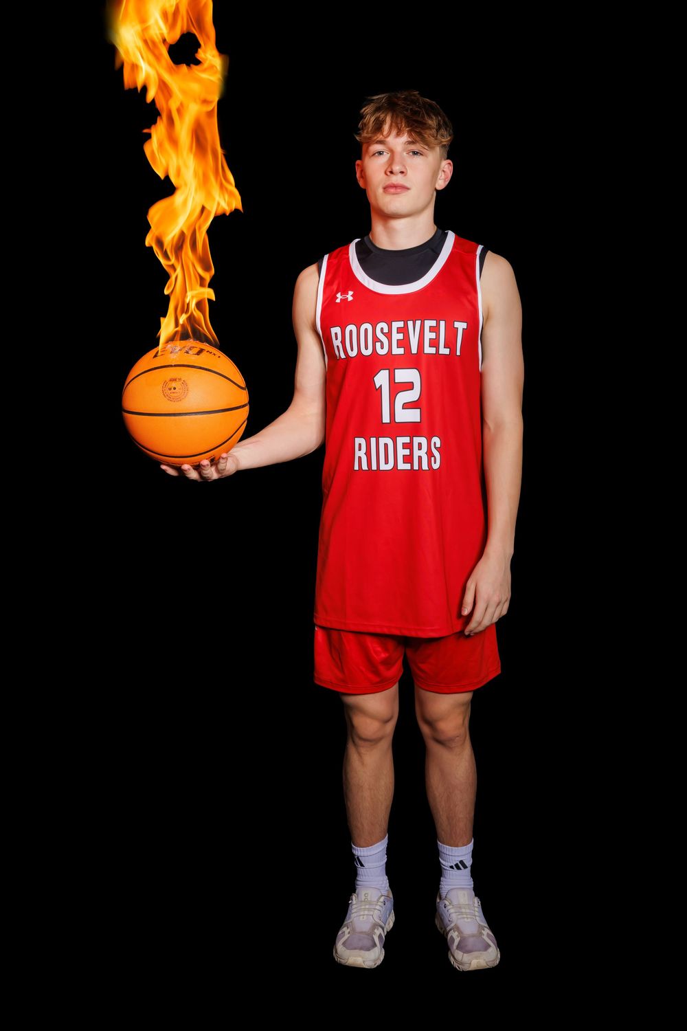 Roosevelt Riders player in red uniform holding flaming basketball against black backdrop.