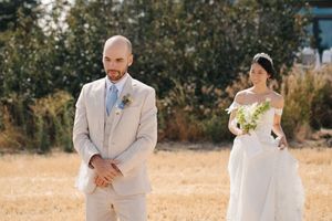 A couple in light-colored wedding attire shares a romantic moment together in a sunlit outdoor setting.