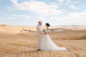 A romantic wedding photoshoot in a golden wheat field under blue skies with rolling hills in the background.