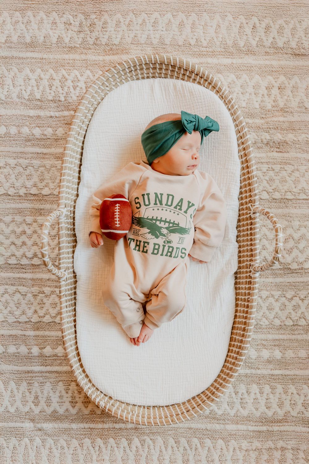 Sleeping newborn baby lies in a basket wearing a green headband and outfit.